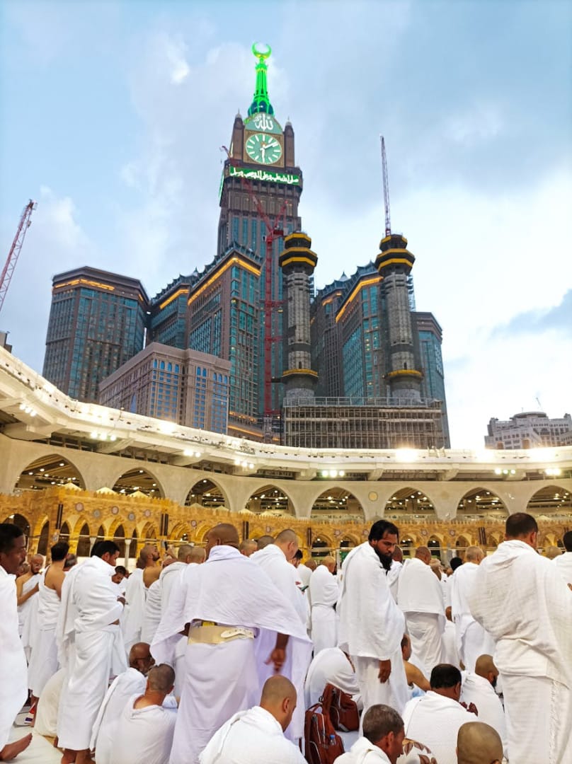 Pilgrims in white robes gather at Abraj Al Bait Towers, Mecca, Saudi Arabia, symbolizing unity and devotion.