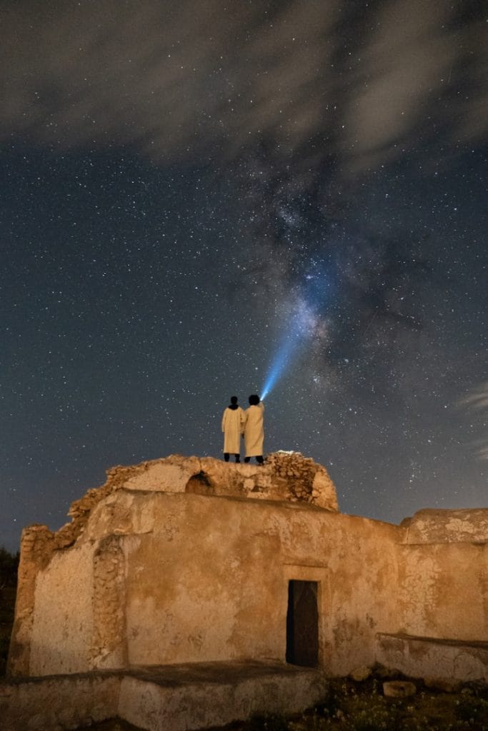 A couple of people standing on top of a building under a night sky