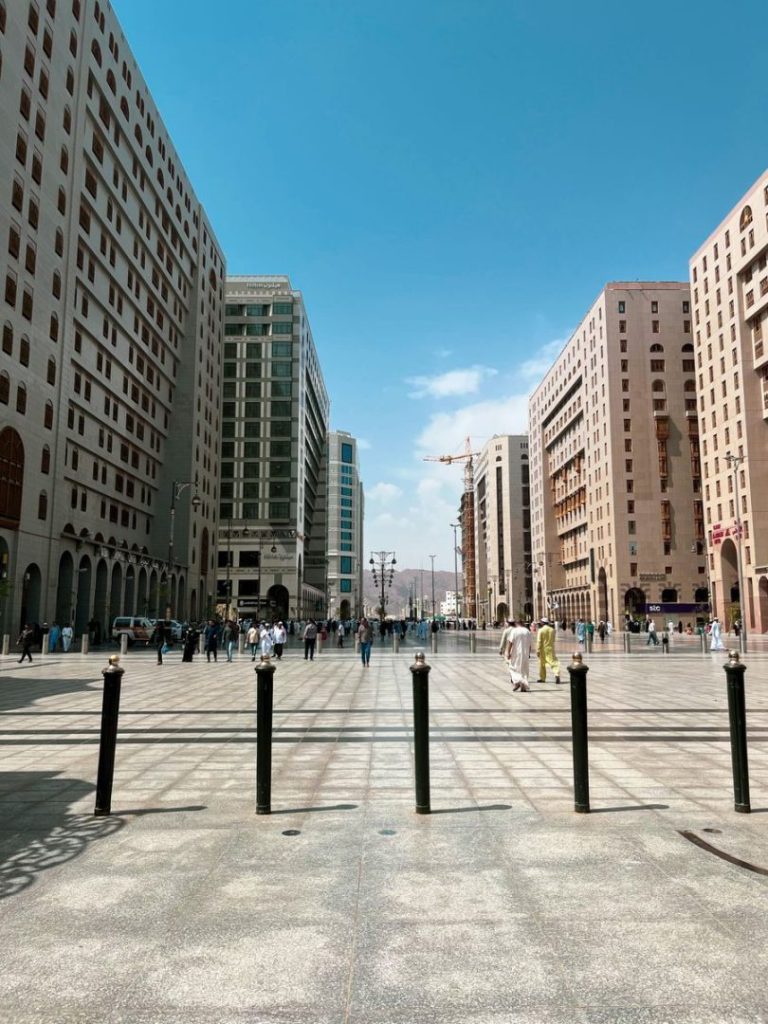 Vibrant urban scene with people walking between tall modern buildings under a clear blue sky.